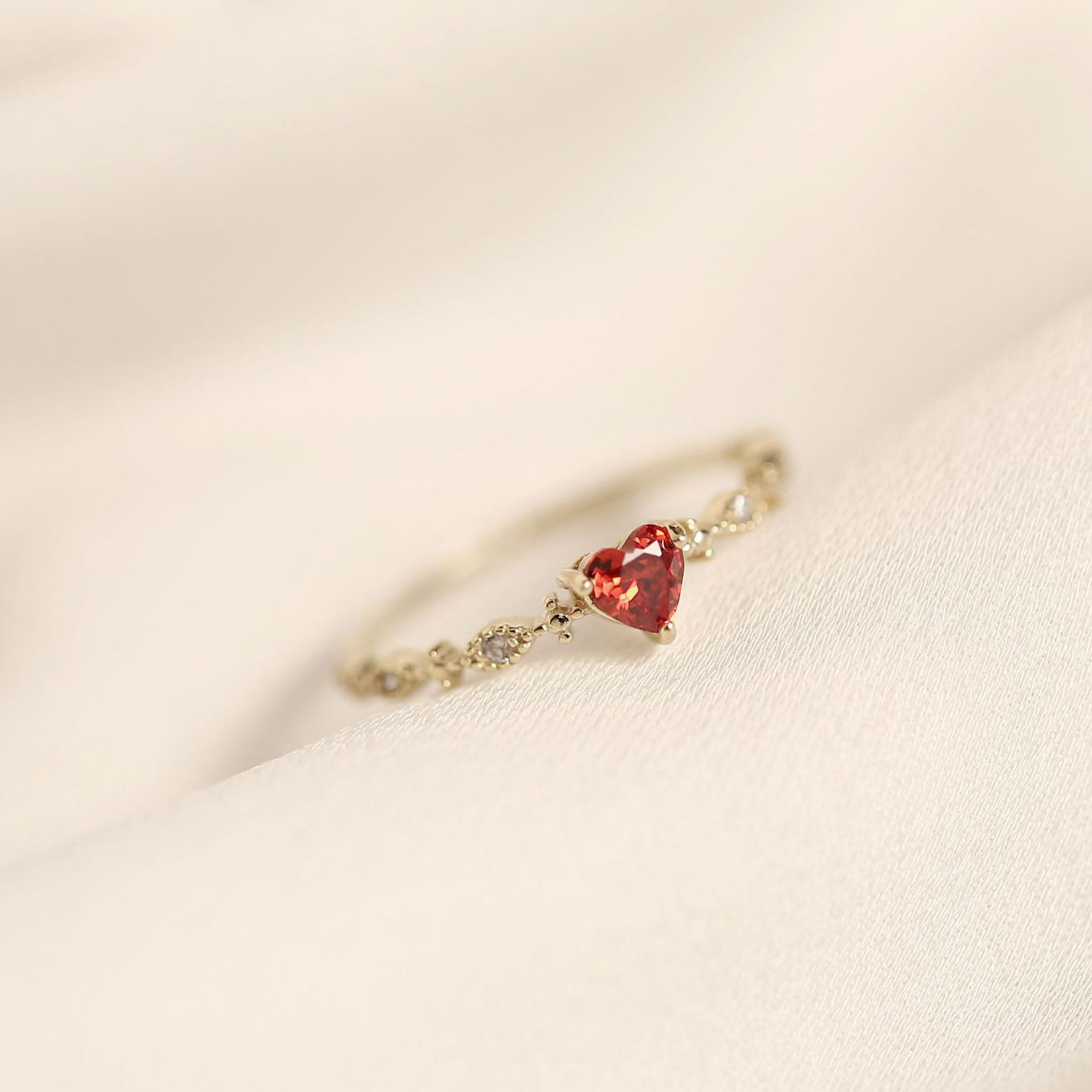 A delicate gold ring with a heart-shaped red gemstone and smaller clear stones on the band.
