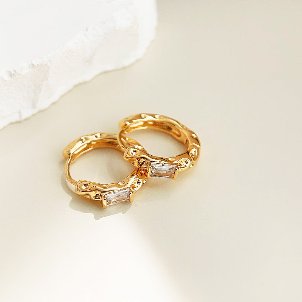 Detailed view of the gold hammered huggie hoop earring with a clear rectangular gemstone