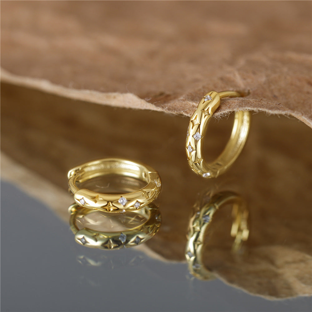 A detailed close-up of the gold hoop earrings with a star and diamond design.