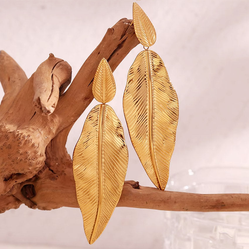 A pair of gold leaf earrings displayed on a piece of driftwood.
