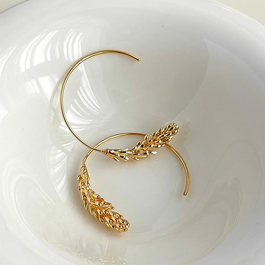 A pair of 14K gold plated brass leaf hoop earrings on a white surface