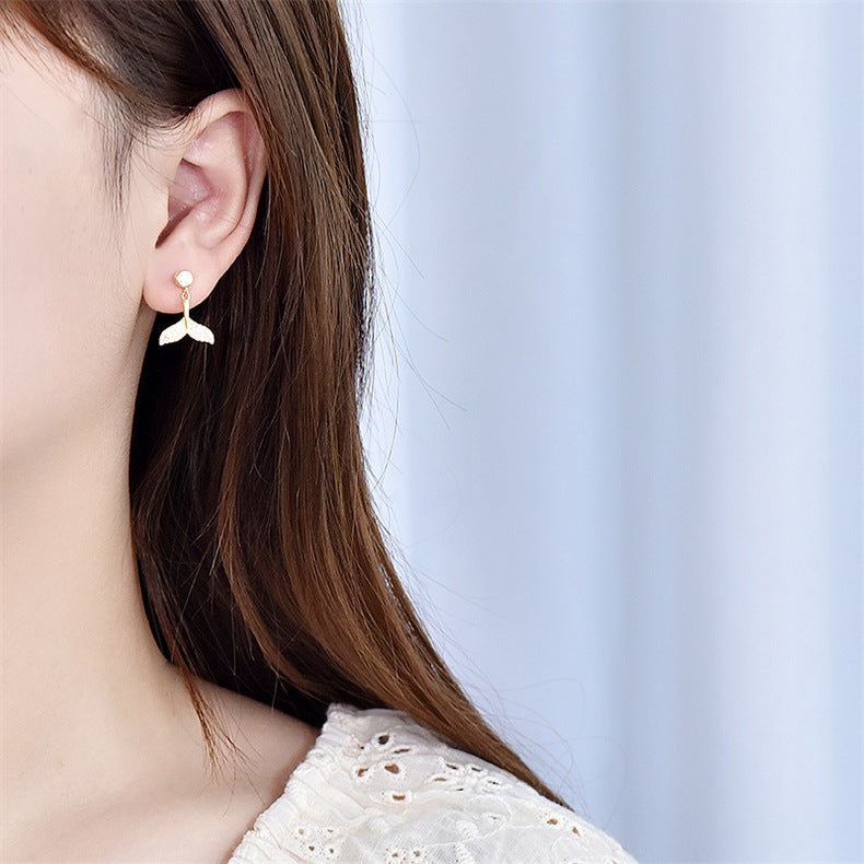 A woman wearing the elegant gold mermaid tail earring, showcasing its delicate design and pearl accent.