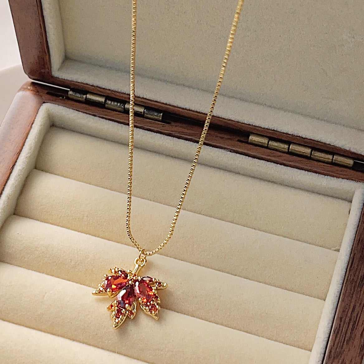 Gold maple leaf necklace presented in a wooden jewelry box