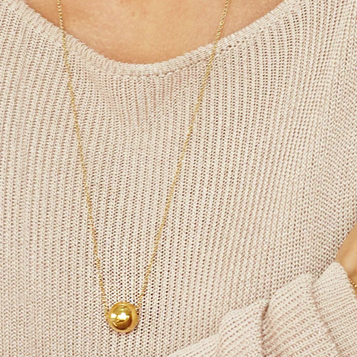 A woman wearing the gold ball pendant necklace with a beige sweater