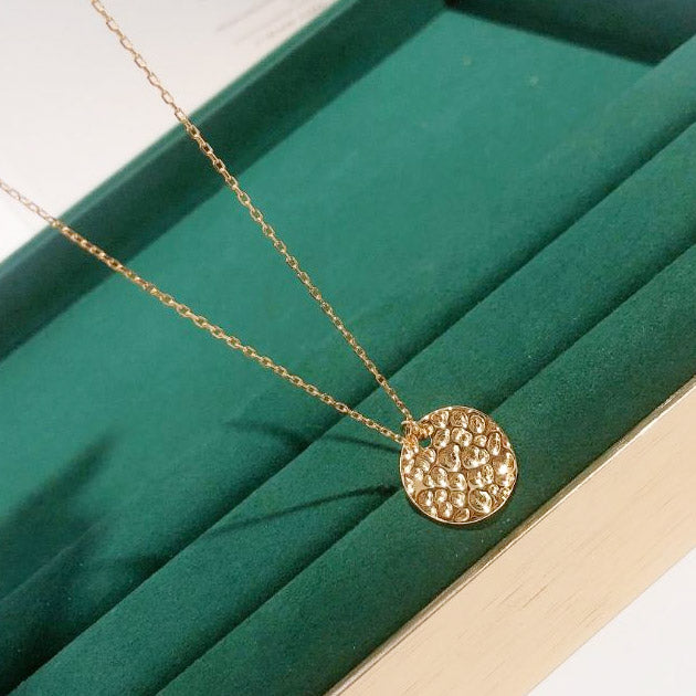 The elegant gold necklace with its textured pendant displayed in a luxurious green velvet jewelry box