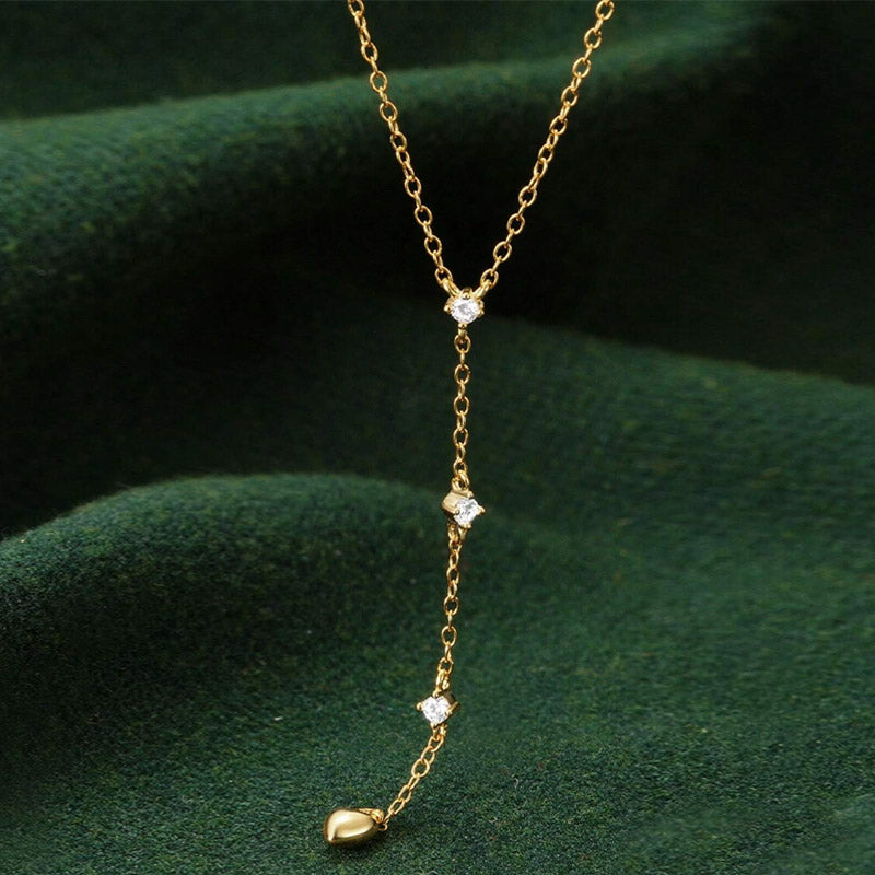 Close-up of the gold Y-shaped heart charm necklace on a dark green background