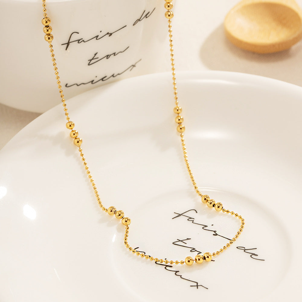 The 18k gold plated beaded necklace displayed on a white plate