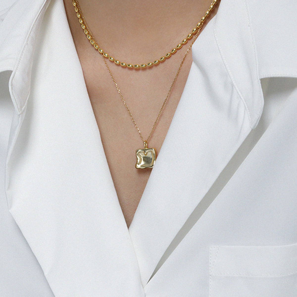A model showcasing the layered look of the 18K gold square charm necklace.