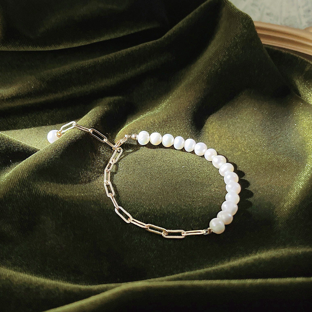A close-up of the 14k gold plated freshwater pearl bracelet showcasing its fine details on a green velvet surface.