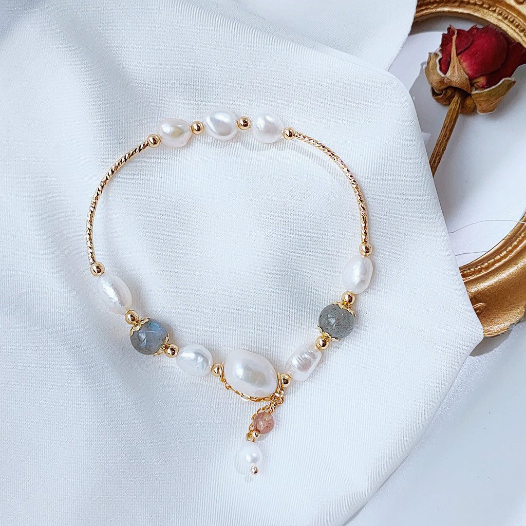 A detailed product shot of the 14k gold plated bracelet set with freshwater pearls and grey stones on a white background.