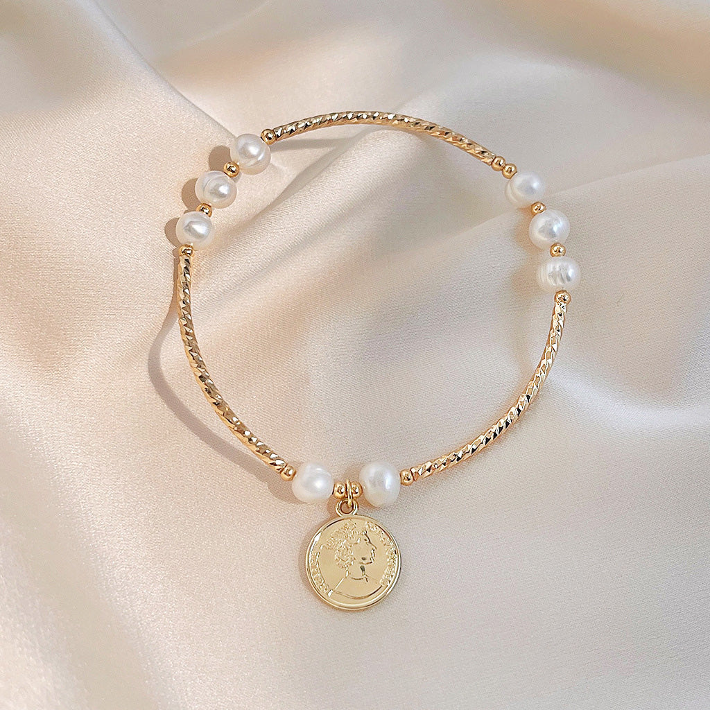 Close-up of the Queen Elizabeth coin charm on the pearl bracelet.