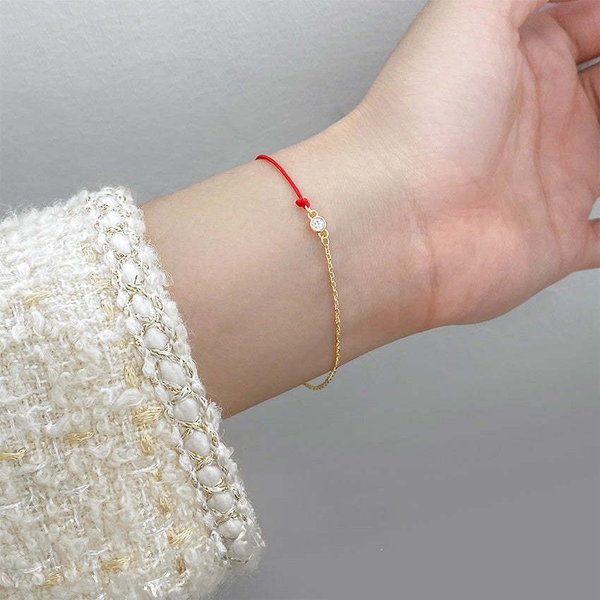 A delicate red string and gold chain cubic zirconia bracelet worn on a wrist.