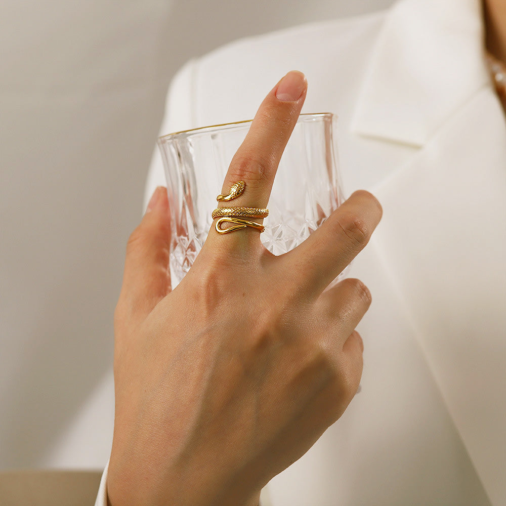 A woman's hand wearing the gold snake ring while holding a glass, showcasing the ring in a lifestyle setting.