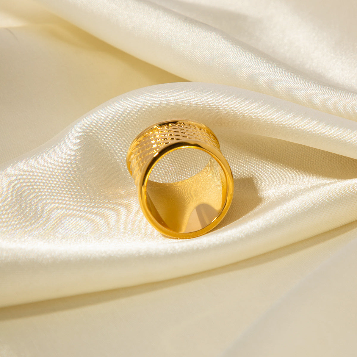 A gold-plated stainless steel ring with a detailed snakeskin texture resting on a soft, cream-colored fabric.