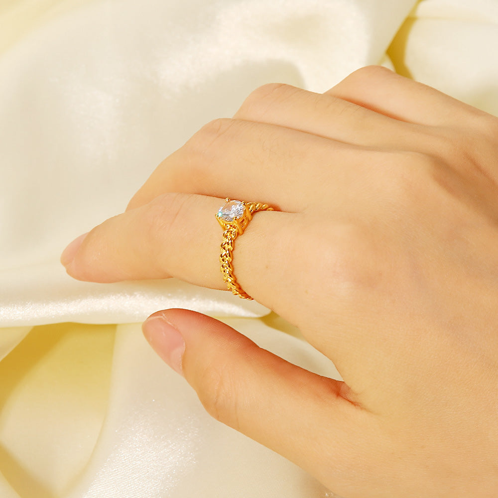 A stylish gold-plated open ring with a clear cubic zirconia stone worn on a finger.