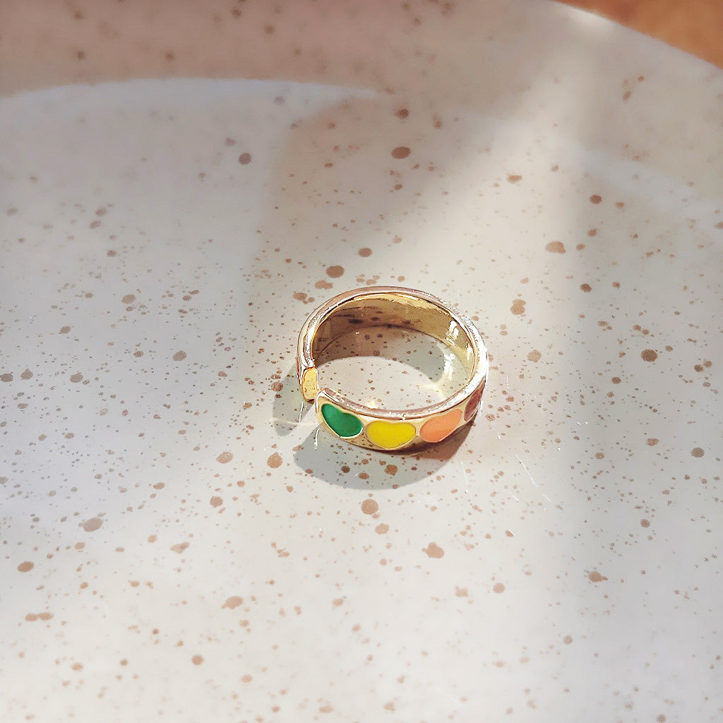 A close-up of a gold-plated open ring with vibrant, multi-colored enamel accents.