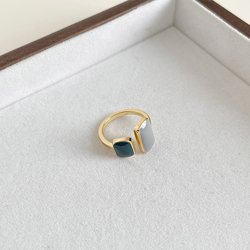 Detailed view of a gold ring with green and gray enamel stones in a jewelry box