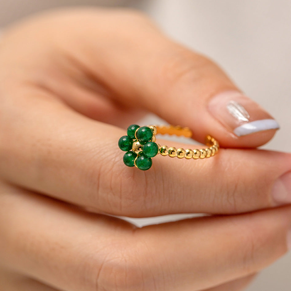 A woman's hand showcasing a gold and green natural stone flower ring.