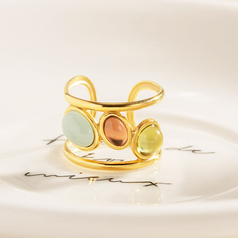 A gold-finished cuff ring with three colorful opal-style stones resting on a decorative plate.