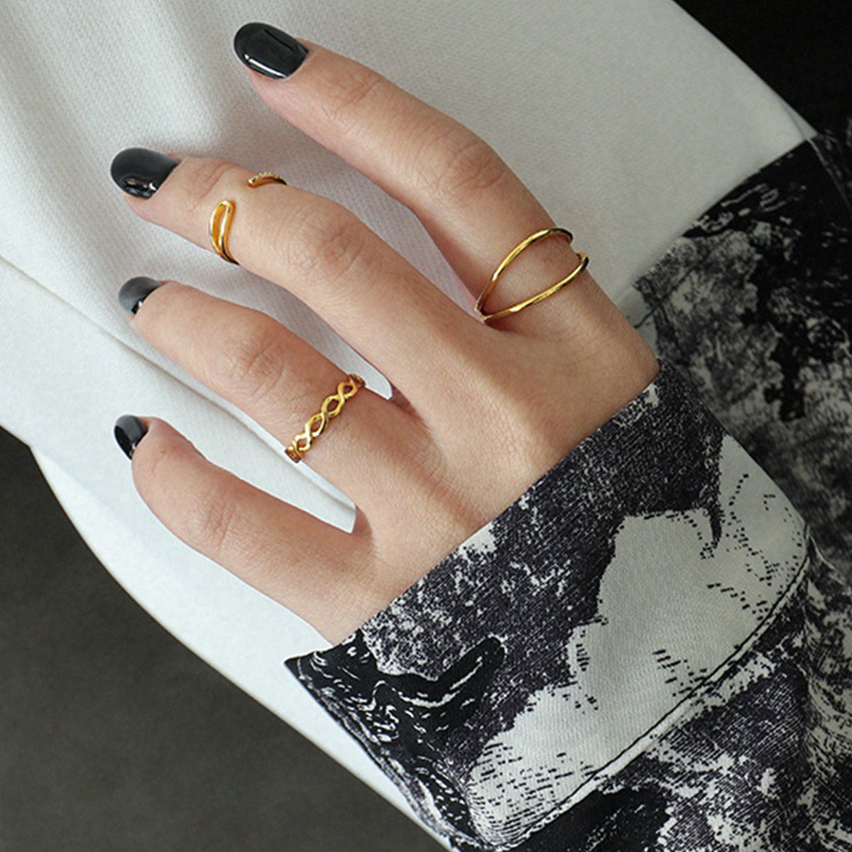 A model's hand with black nails showcasing the set of 5 gold minimalist double line rings.