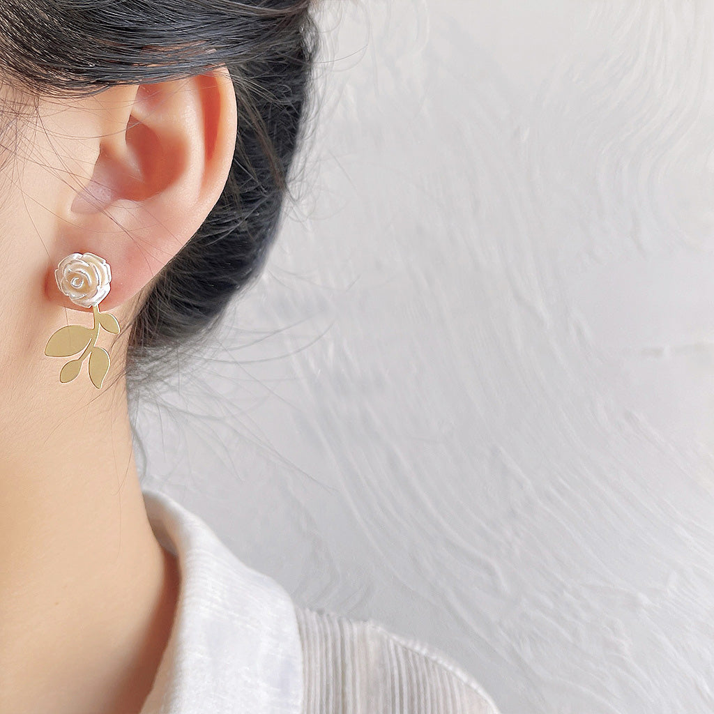 Detailed close-up of the 3D white rose earring with gold leaf accents.