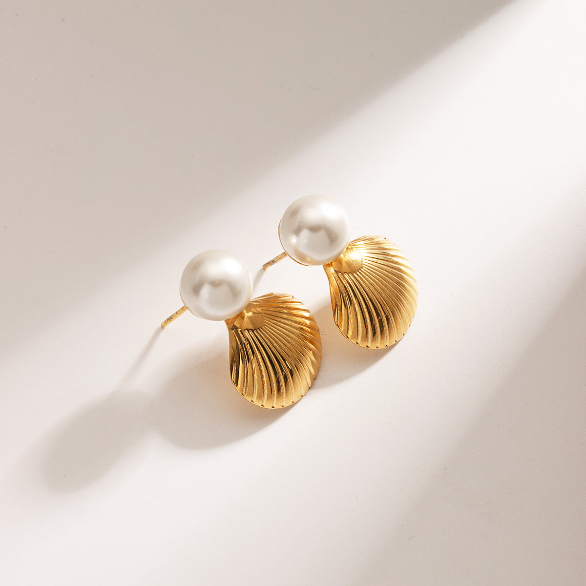 A pair of stainless steel gold shell earrings with pearls displayed