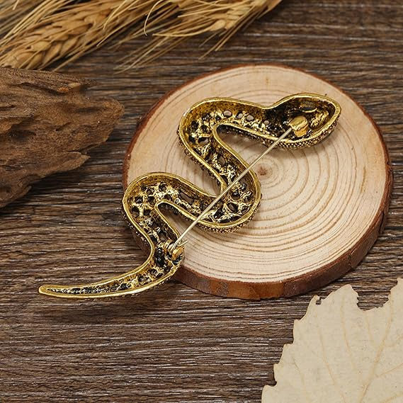 A detailed gold snake brooch with a textured finish displayed on a wooden surface.