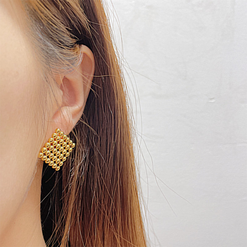 A woman wearing the gold square beaded stud earring to show its scale and style.