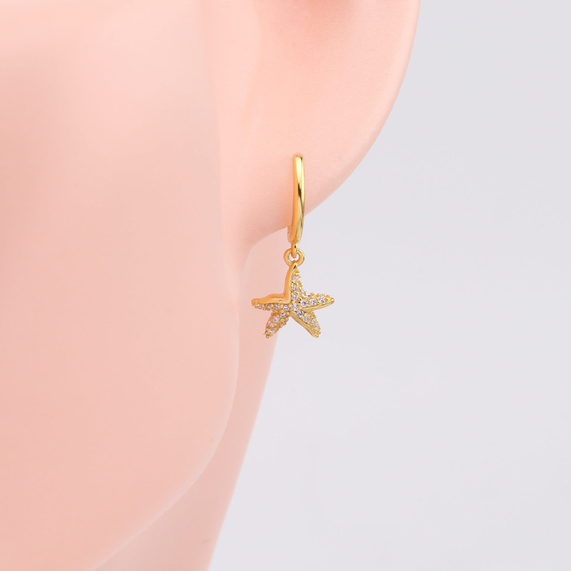 A detailed close-up of a gold starfish huggie earring showcasing its intricate design and gemstone details.