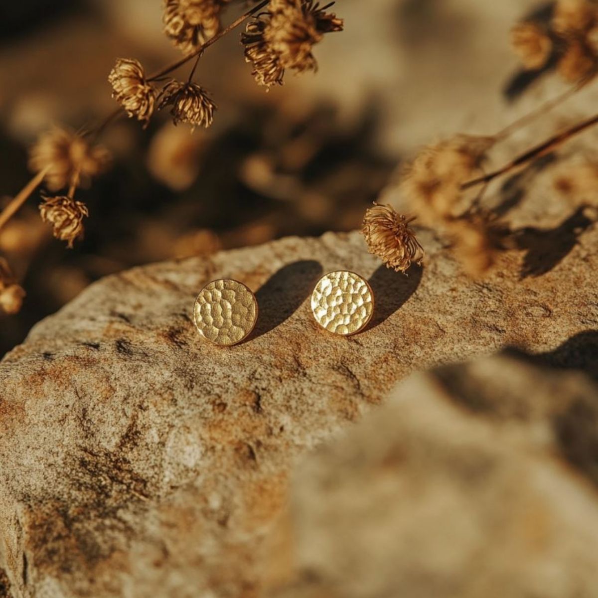 A pair of stylish gold-textured PVD plated stainless steel earrings displayed on a stone.