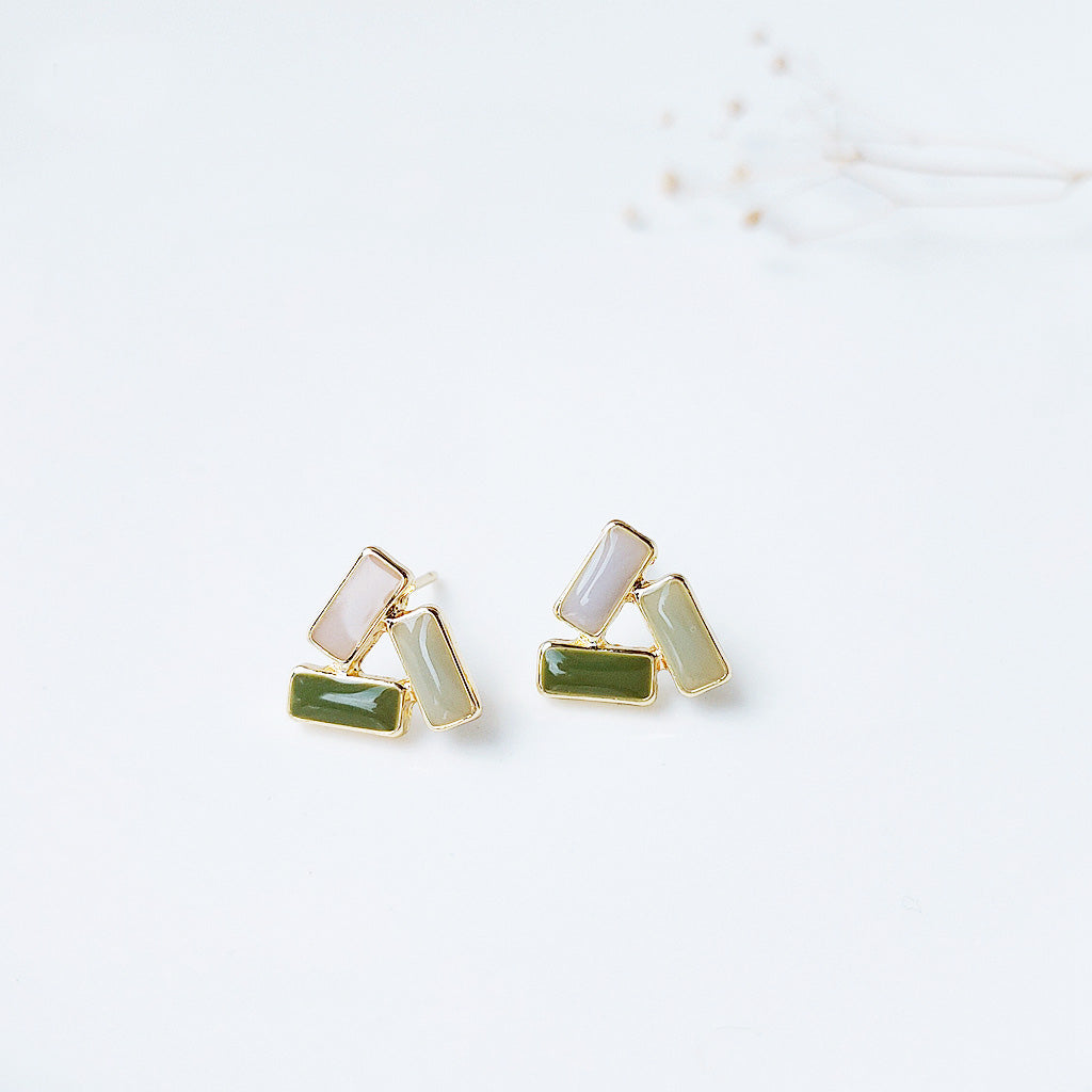 Close-up of gold-plated triangular stud earrings with green and white enamel stones.
