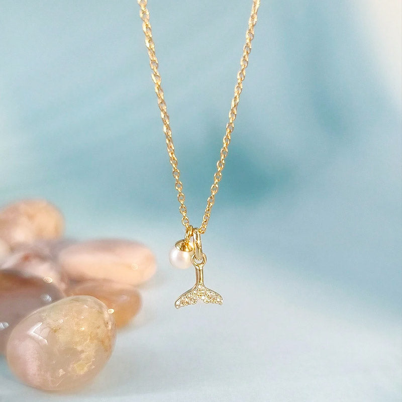 Detailed view of the zircon whale tail pendant with a pearl on a gold chain