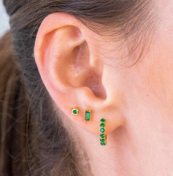 A close-up of the Emerald Huggie Hoop Earrings being worn, showing their elegant look on the ear.