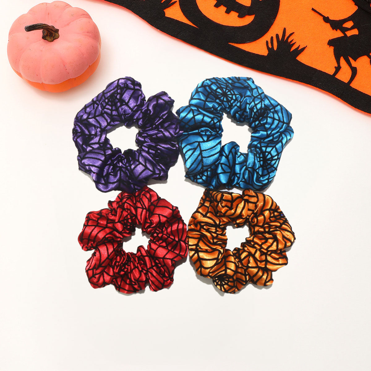 A collection of Halloween spiderweb scrunchies in purple, blue, red, and orange