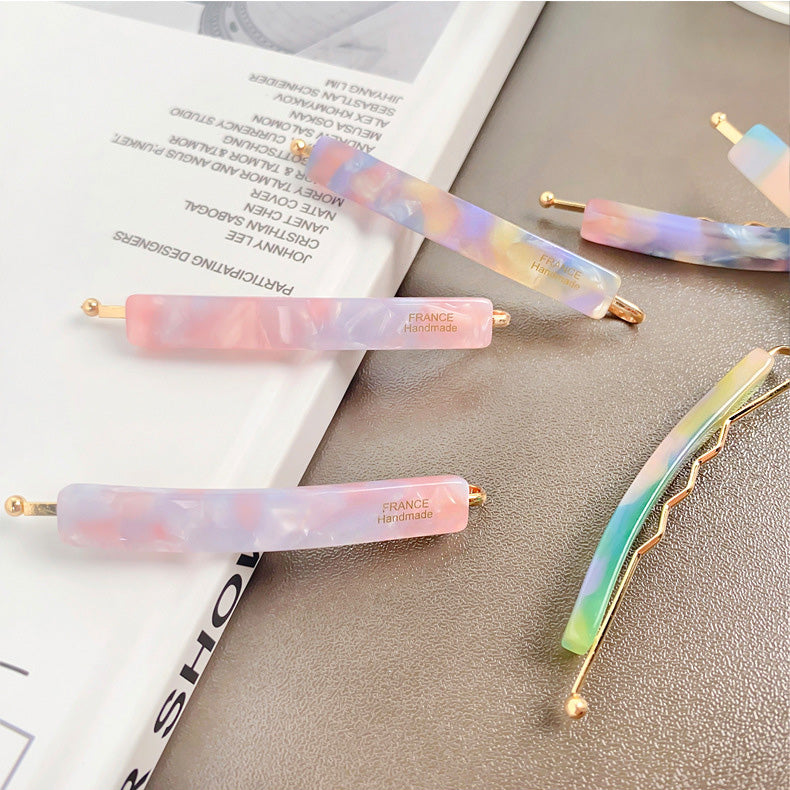A pair of handmade marbled acetate hair clips with gold accents.