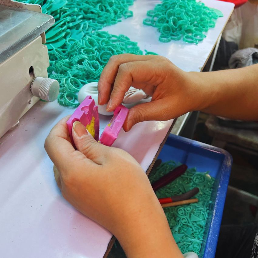 A close-up of a technician's hands shaping a pink wax model for jewelry.