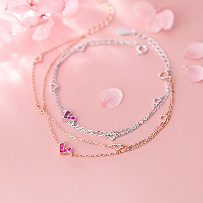 Stylish heart charm bracelets made from 925 sterling silver, showcased against a soft pink background.