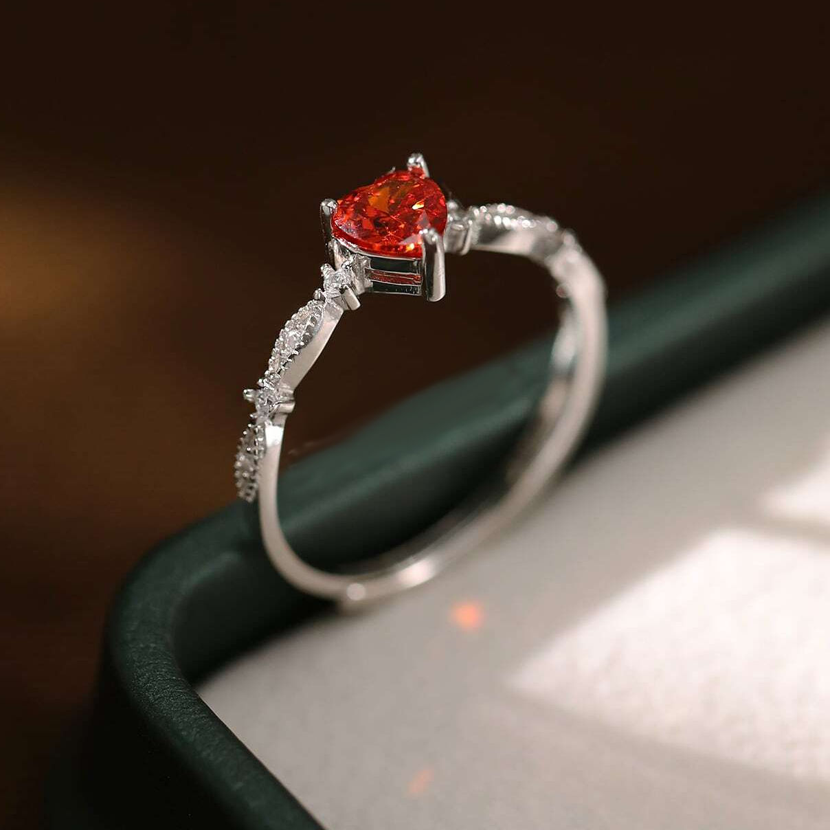 A silver ring with a heart-shaped orange gemstone, displayed in a ring box.