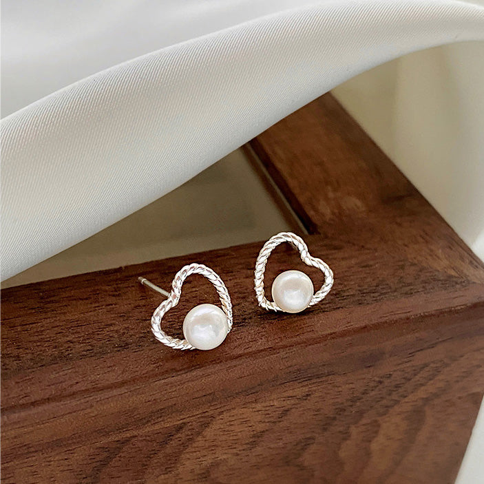 A flat lay of the 925 sterling silver hollow heart pearl earrings on a white fabric background.