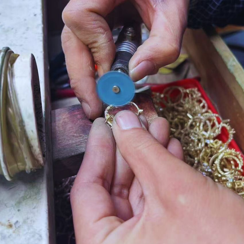 A jeweler using a specialized tool for precision polishing on a gold jewelry piece.