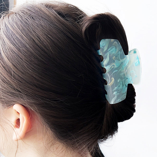 A model showcasing the secure hold of a light blue acetate hair clip in her bun.