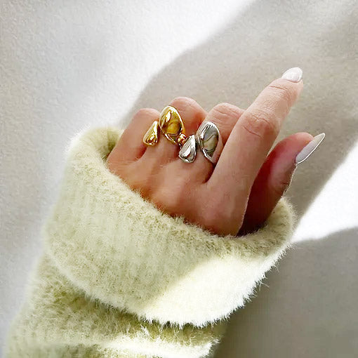 Hand model with leaf-inspired asymmetric rings in gold and silver.