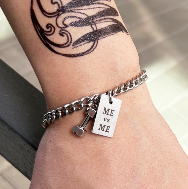 Close-up view of the 'ME vs ME' charm on the stainless steel dumbbell bracelet.