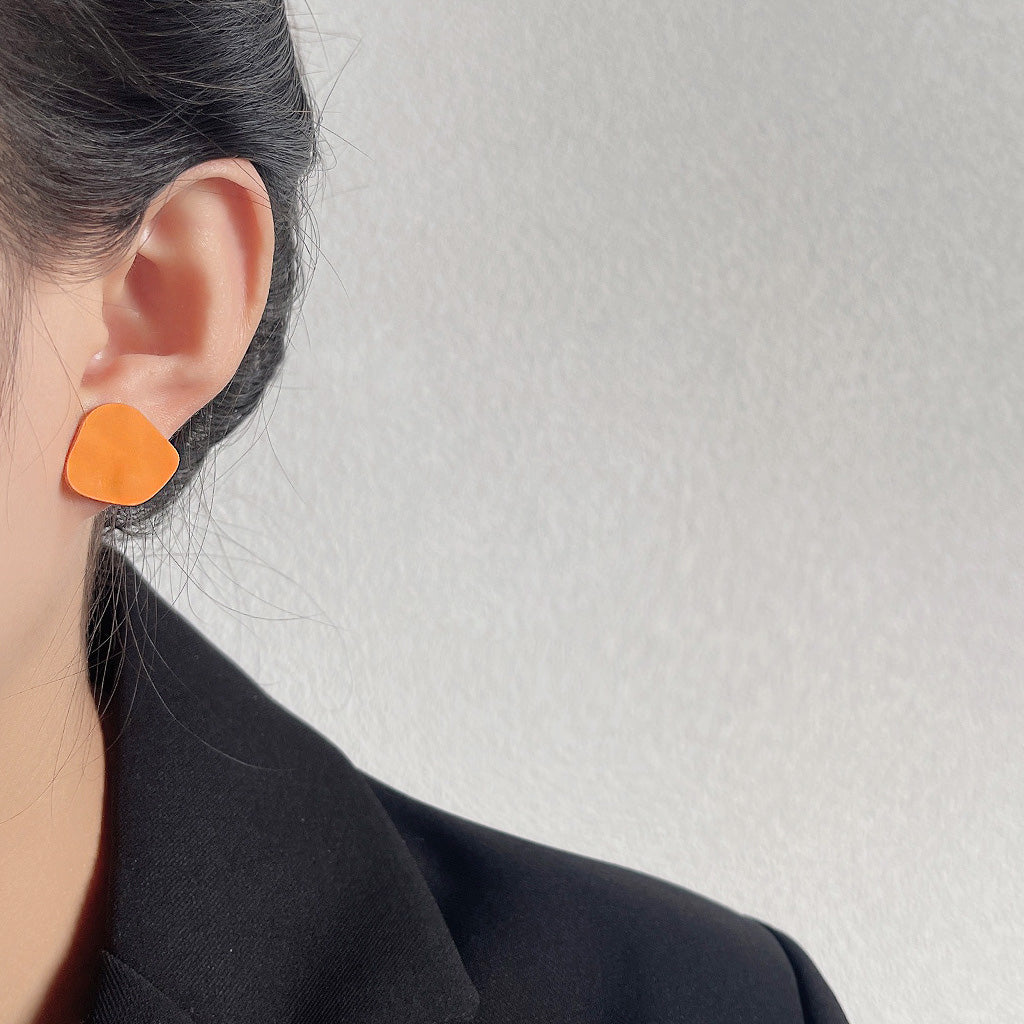 A model wearing the vibrant orange matte enamel stud earring.