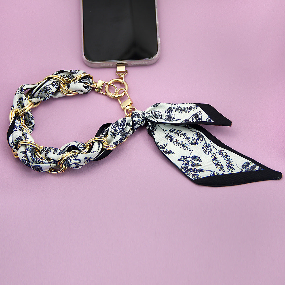 A detailed view of the floral print silk scarf phone strap showing the gold hardware.