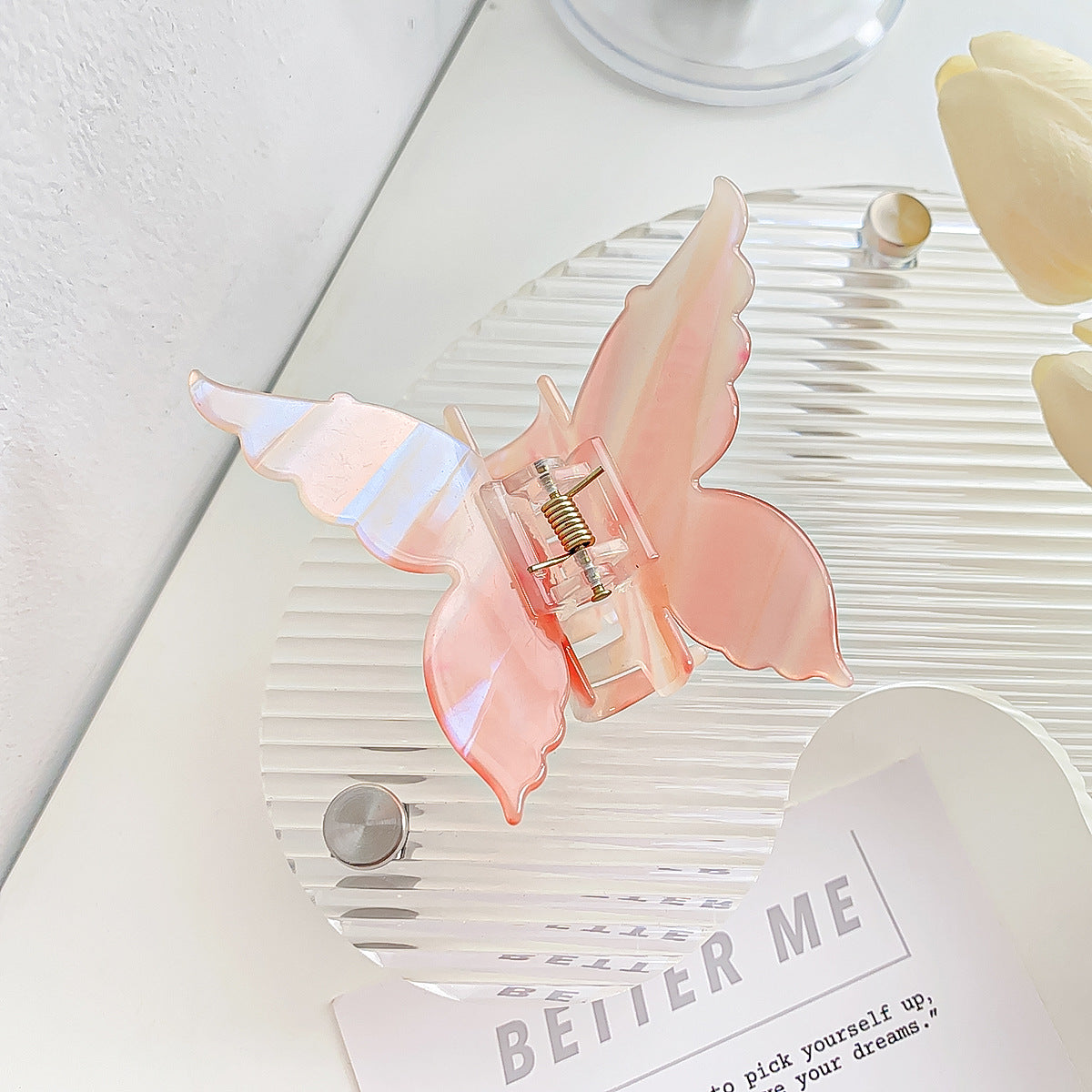 A pink butterfly hair clip held up to show its translucent quality and striped design.