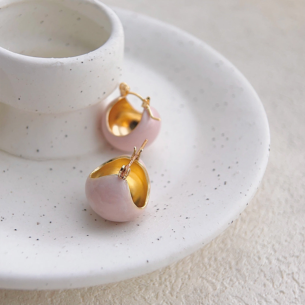 A pair of pink and gold spherical earrings displayed on a decorative plate.