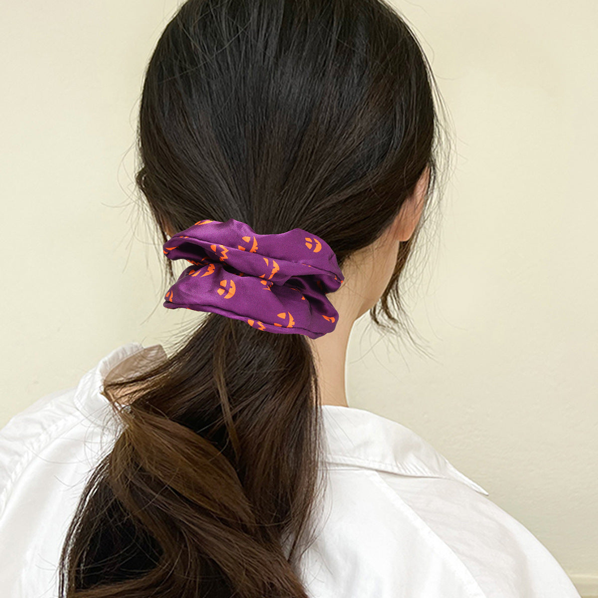 A purple Halloween scrunchie with jack-o'-lanterns styling a ponytail