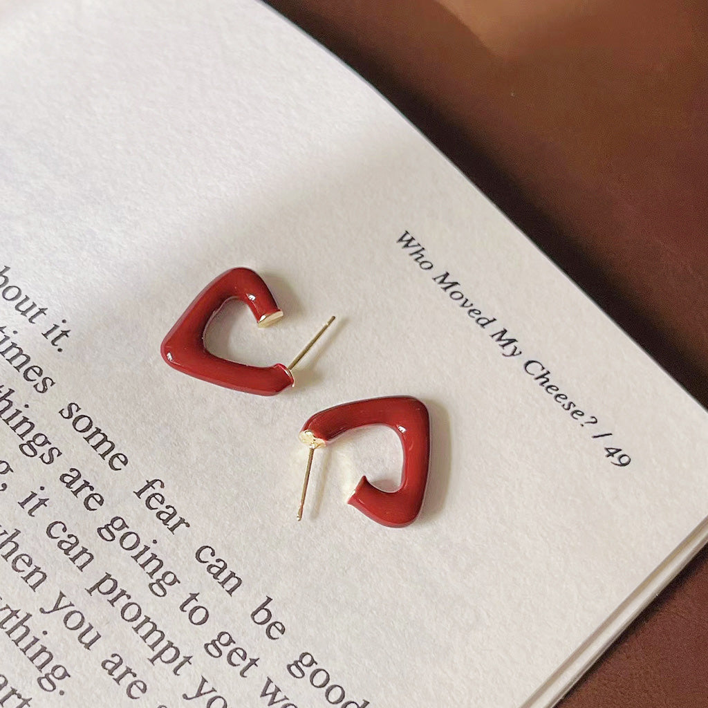 A set of red enamel C-shape and heart-shaped earrings displayed stylishly on a book.