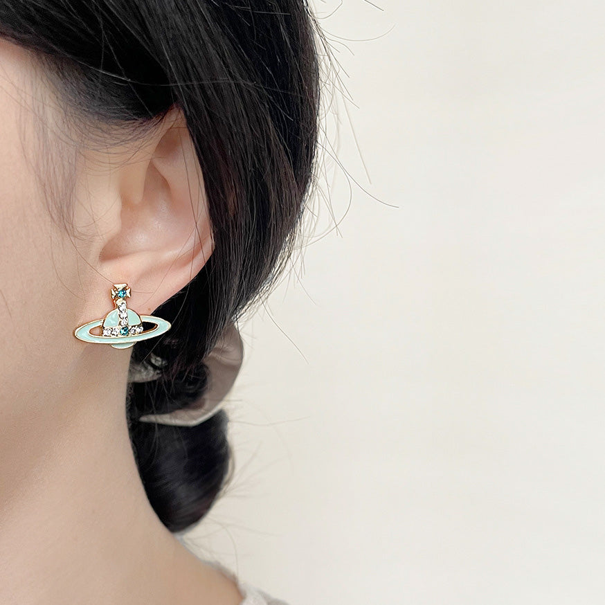 A woman wearing the light blue enamel planet stud earring to show its scale and appearance.